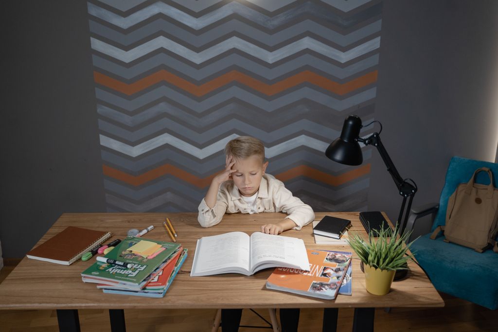 A young boy sitting at a desk, focused on his homework surrounded by school supplies.